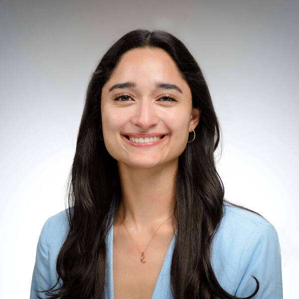 Smiling women with long dark hair, wearing a light blue colored coat..